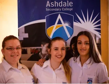 Three students smiling in front of an Ashdale Secondary College banner
