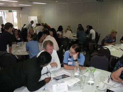 Health professionals collaborating in small groups at round tables during a scenario planning workshop