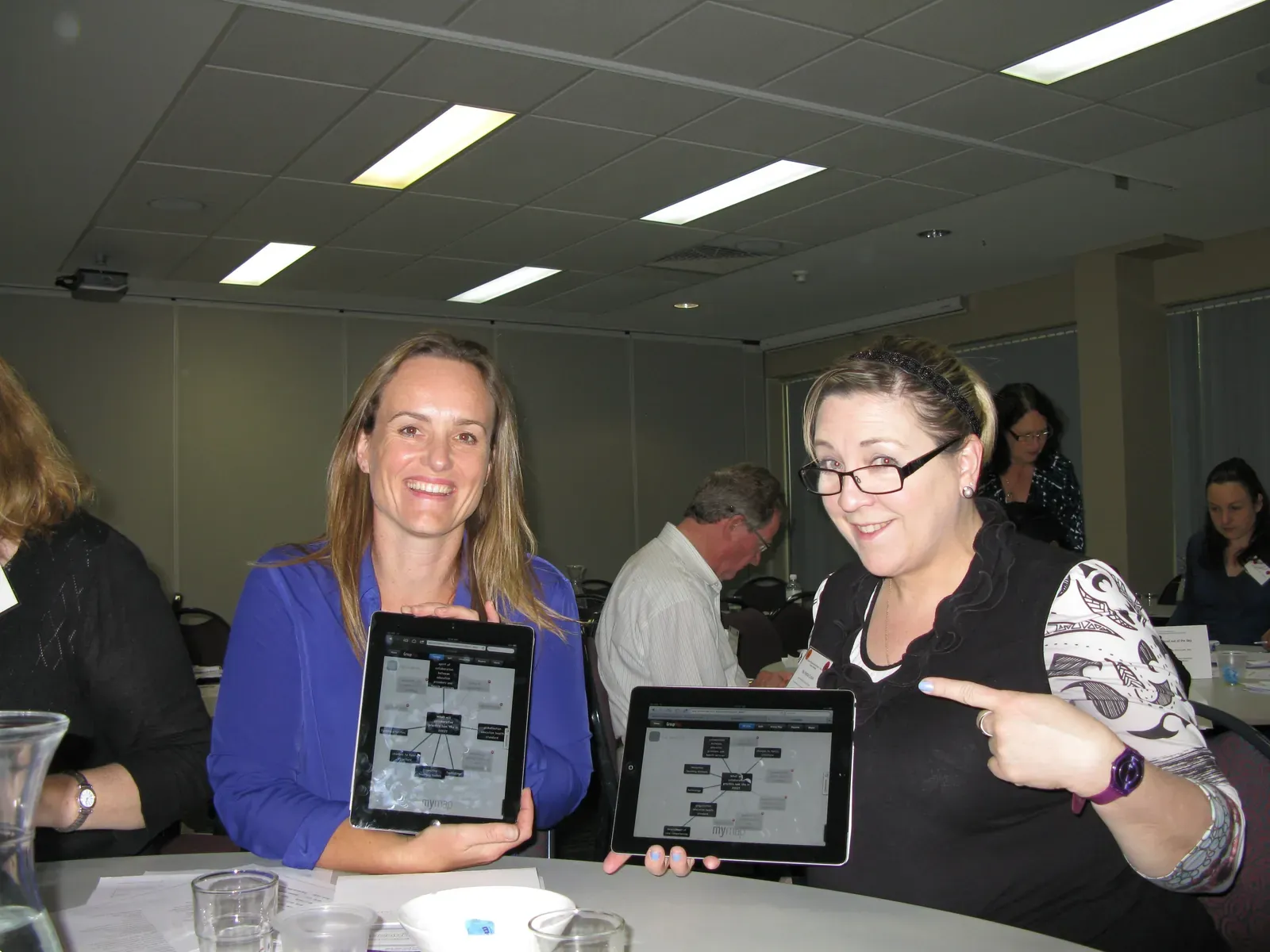 Two women holding tablets showing GroupMap mind maps at a workshop