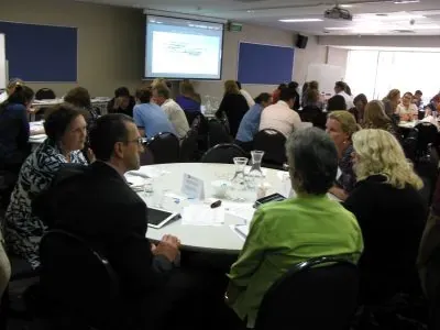 Workshop participants seated at round tables facing a presentation screen at the front