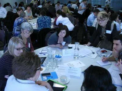 A busy workshop room of participants brainstorming in groups at round tables