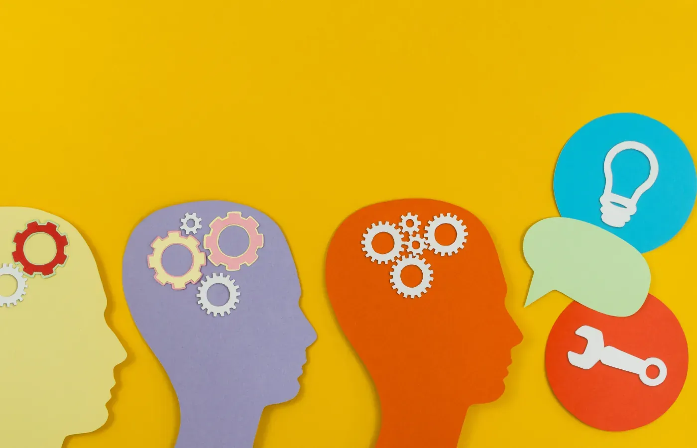 Paper cut-out profiles of heads with gears and a lightbulb representing ideas