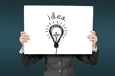 Person in a suit holding a sign with a hand-drawn light bulb and the word idea