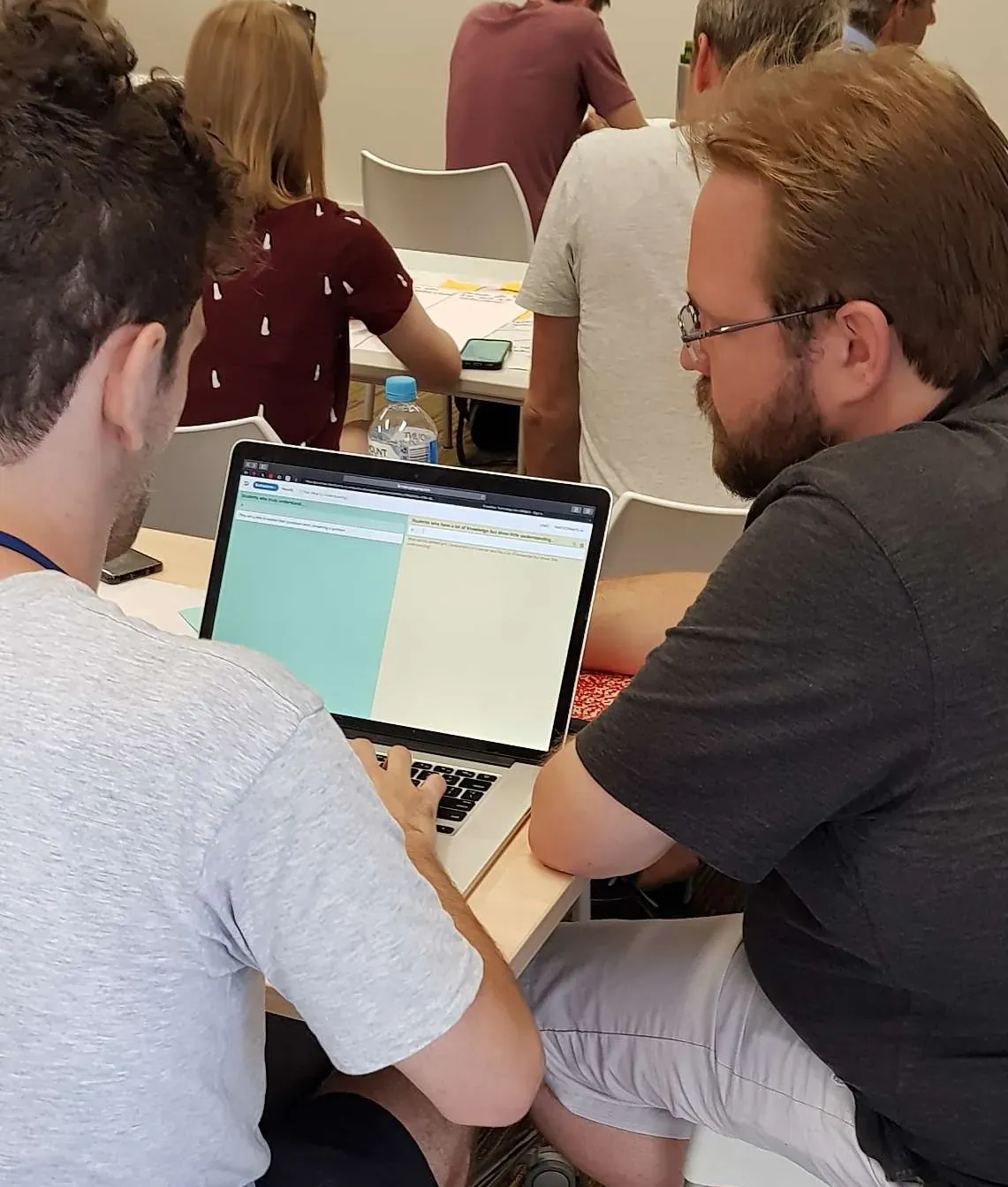 Two workshop participants collaborating over a laptop showing a two-column GroupMap board