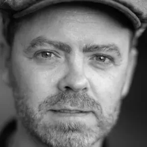 Black and white headshot of workshop facilitator Jonathan Nalder wearing a flat cap