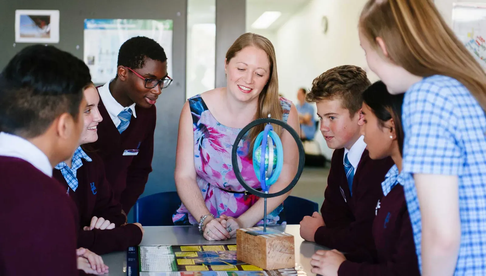 Smiling teacher and uniformed high school students gathered around a science model on a table