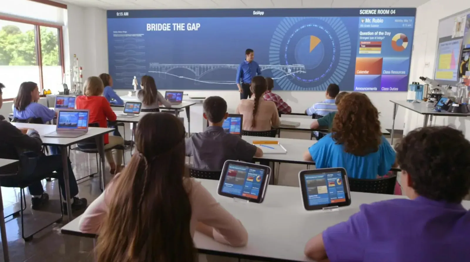 Students using laptops and tablets in a modern classroom facing a large display
