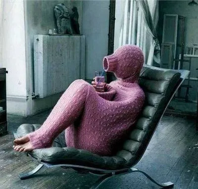 Person hidden inside a full-body knitted sweater relaxing in a chair