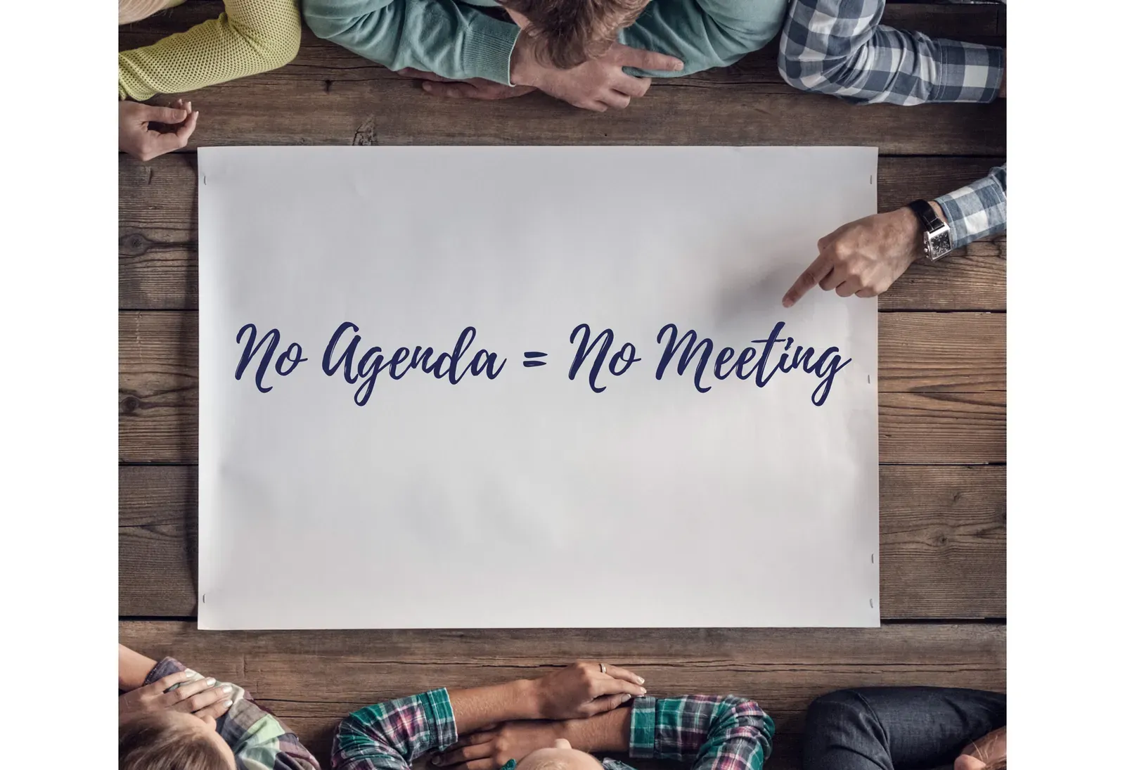 Overhead view of people around a table with a sign reading No Agenda equals No Meeting