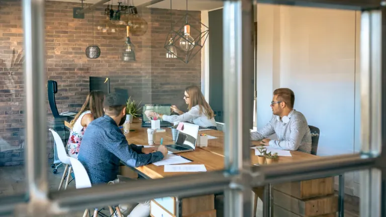 Team meeting around a table with laptops seen through glass walls