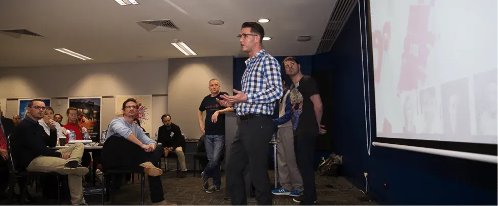 Hackathon judges and participants seated at tables using iPads during the team pitches