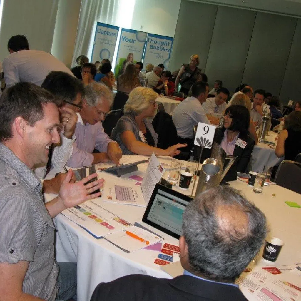 Conference participants collaborating at tables using laptops during the innovation workshop