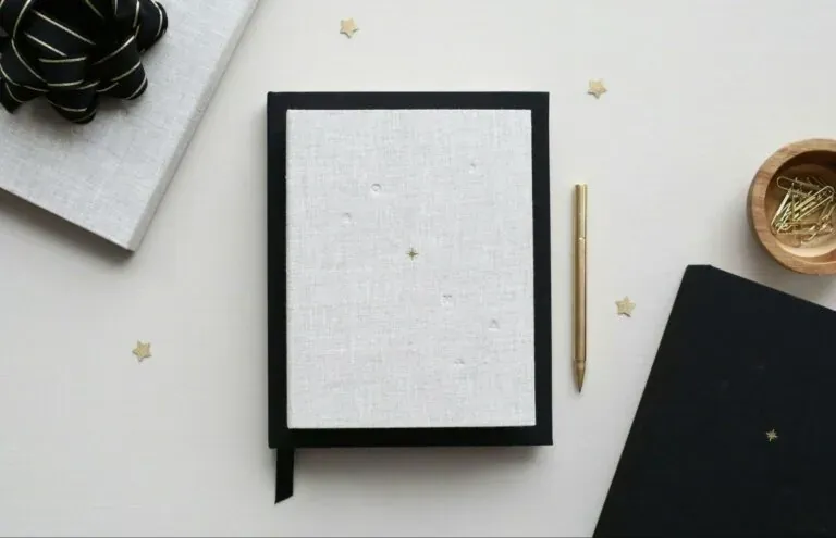 Linen covered notebook gold pen and star confetti laid out ready for planning a meeting agenda