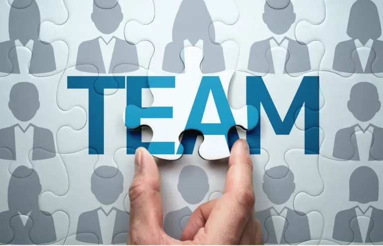 Hand placing a puzzle piece to complete the word TEAM over people silhouettes