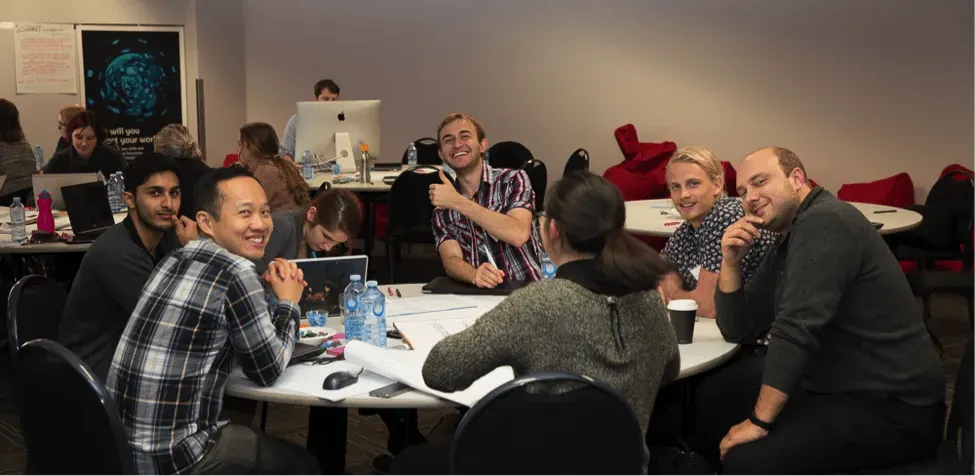 Smiling hackathon team around a table with one member giving a thumbs up