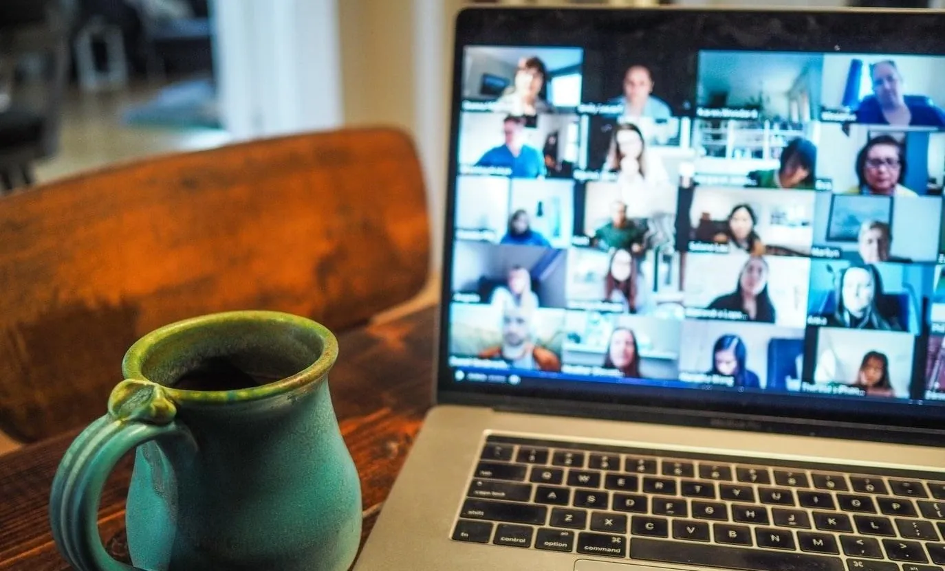 Laptop showing a video call with many participants beside a coffee mug