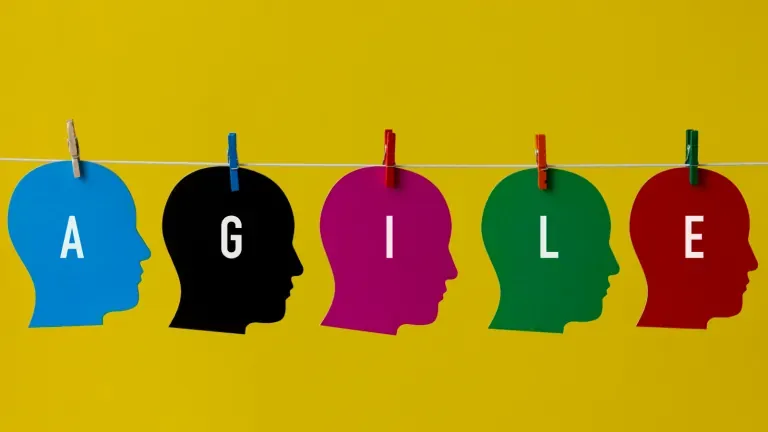 Five colorful paper head silhouettes pegged on a line spelling the word AGILE