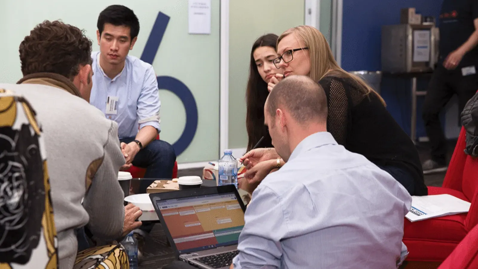 Workshop participants gathered around a low table in discussion, with a GroupMap board open on a laptop between them